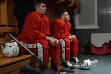 Two ice hockey players in red uniforms relaxing in a locker room, preparing for the game.