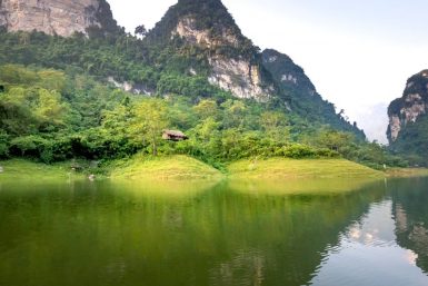 Amazing landscape of calm Na Hang lake surrounded by huge rocky mountains covered with green trees on sunny day in Tuyen Quang province